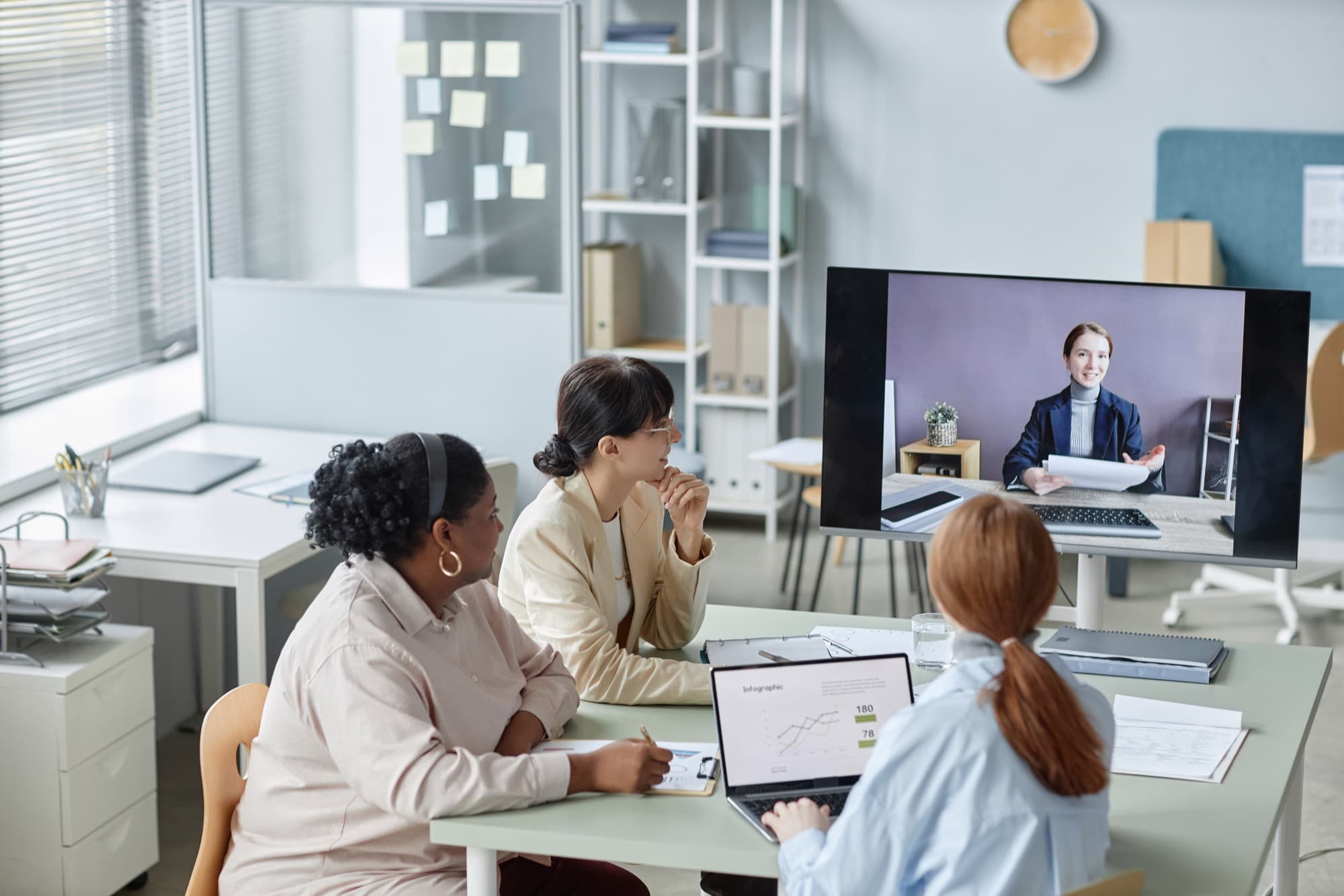 Three people watching a presenter on a wall-mounted screen